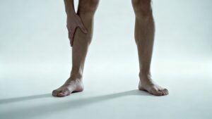 person standing barefoot with flat feet alignment and touching shin illustrating connection between flat feet and shin splints