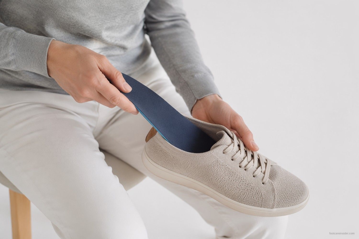 Person inserting a slim supportive insole into a narrow athletic shoe in a clean healthcare editorial setting.
