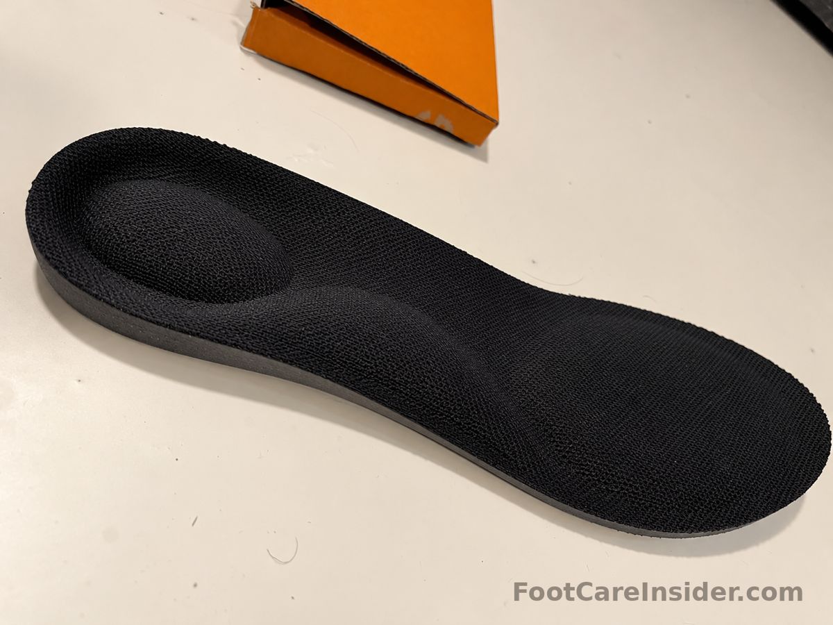 Black textured insole with a contoured heel cup on a cream surface