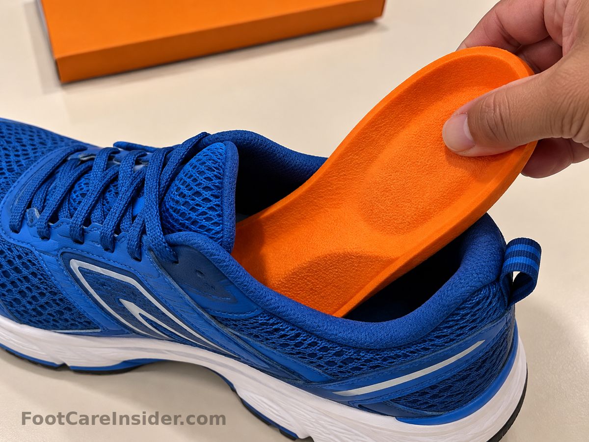Hand placing an orange insole into a blue running shoe