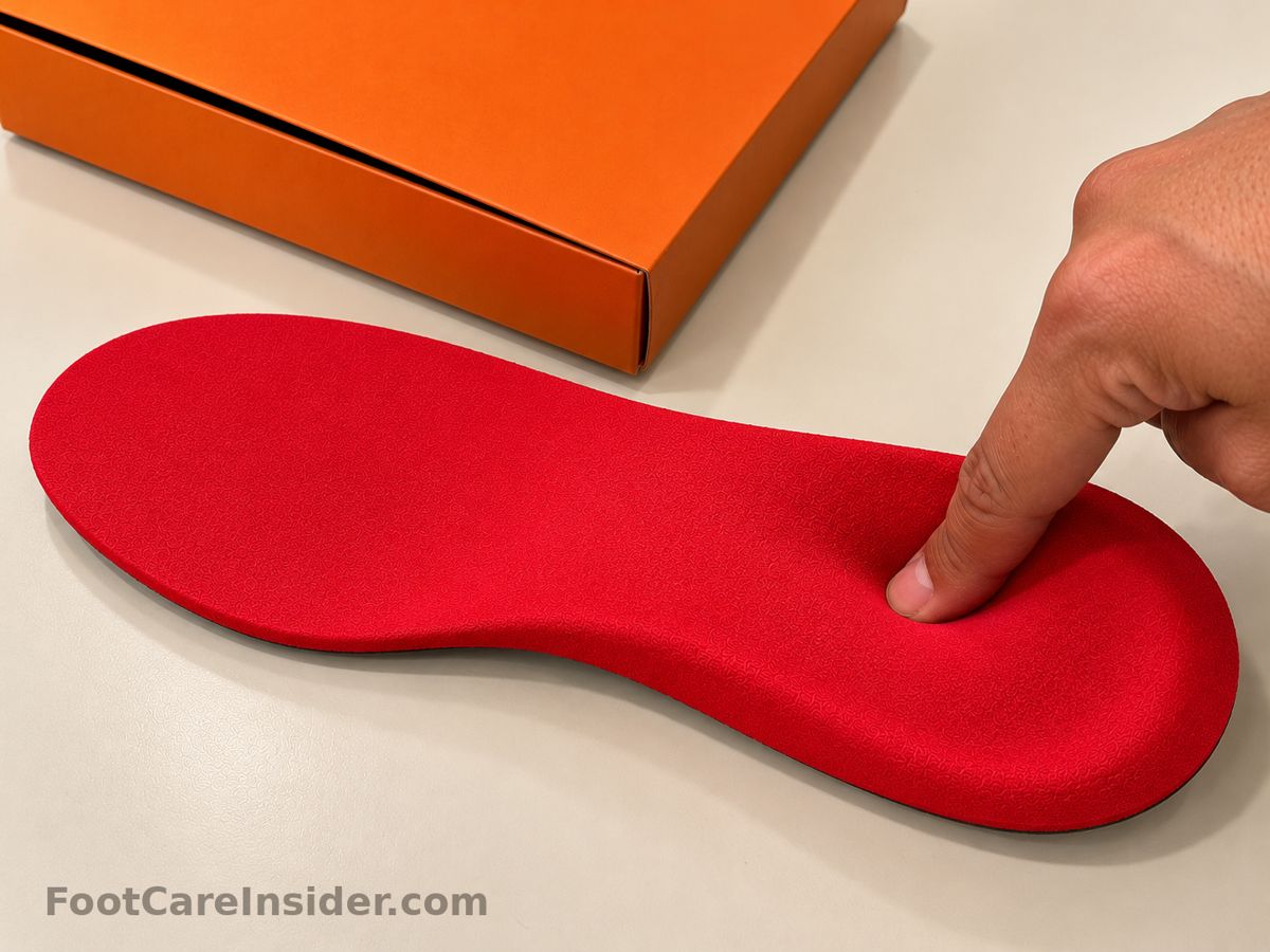 Finger pressing a red foam insole next to an orange box